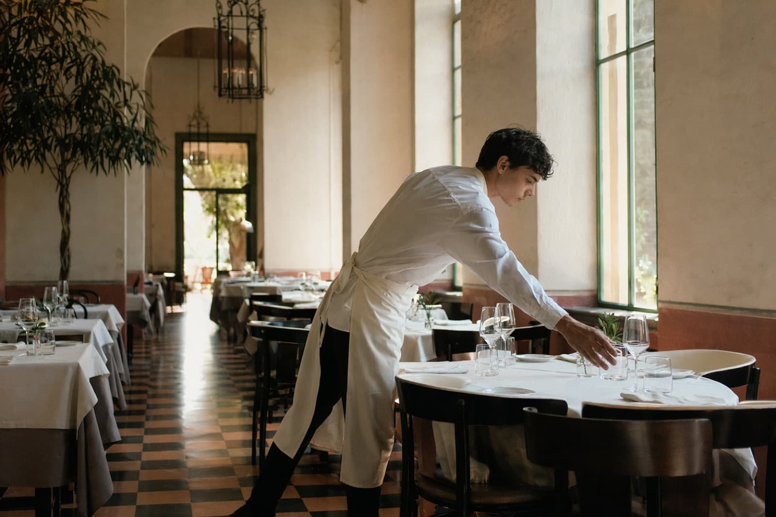 Nel primo pomeriggio, con un cameriere in meno per il turno, il telefono in cassa squilla mentre la sala del ristorante va preparata comunque