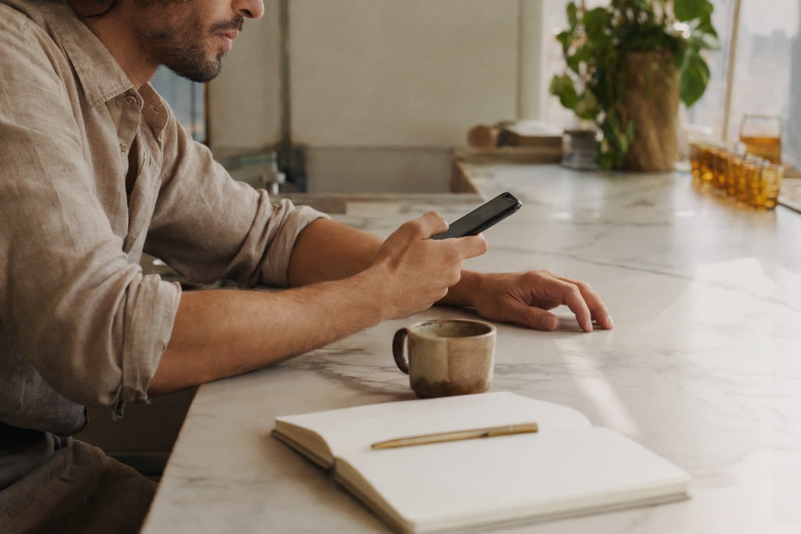Le mani di un ristoratore al bancone del bar scrivono un messaggio al telefono, accanto a un taccuino e un caffè